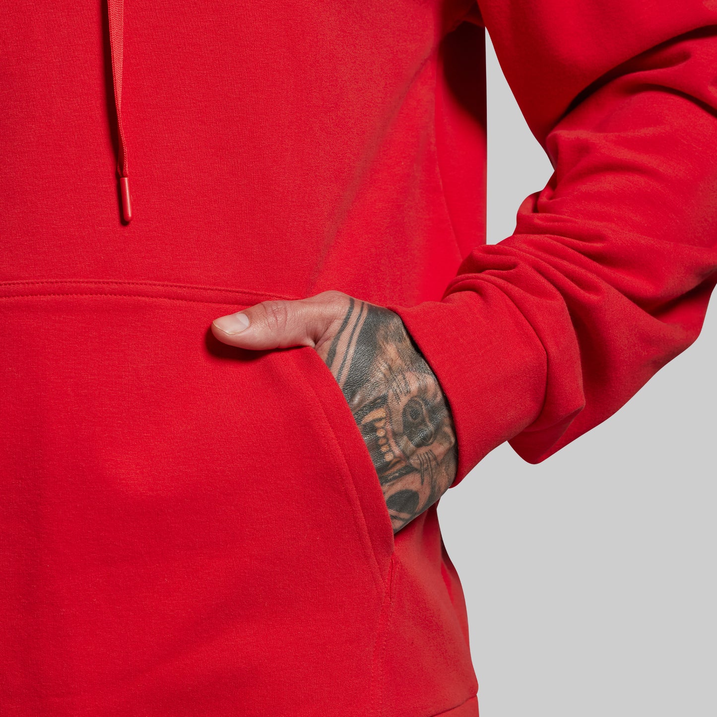 Red hoodie worn by a person with tattooed arm on a gray background