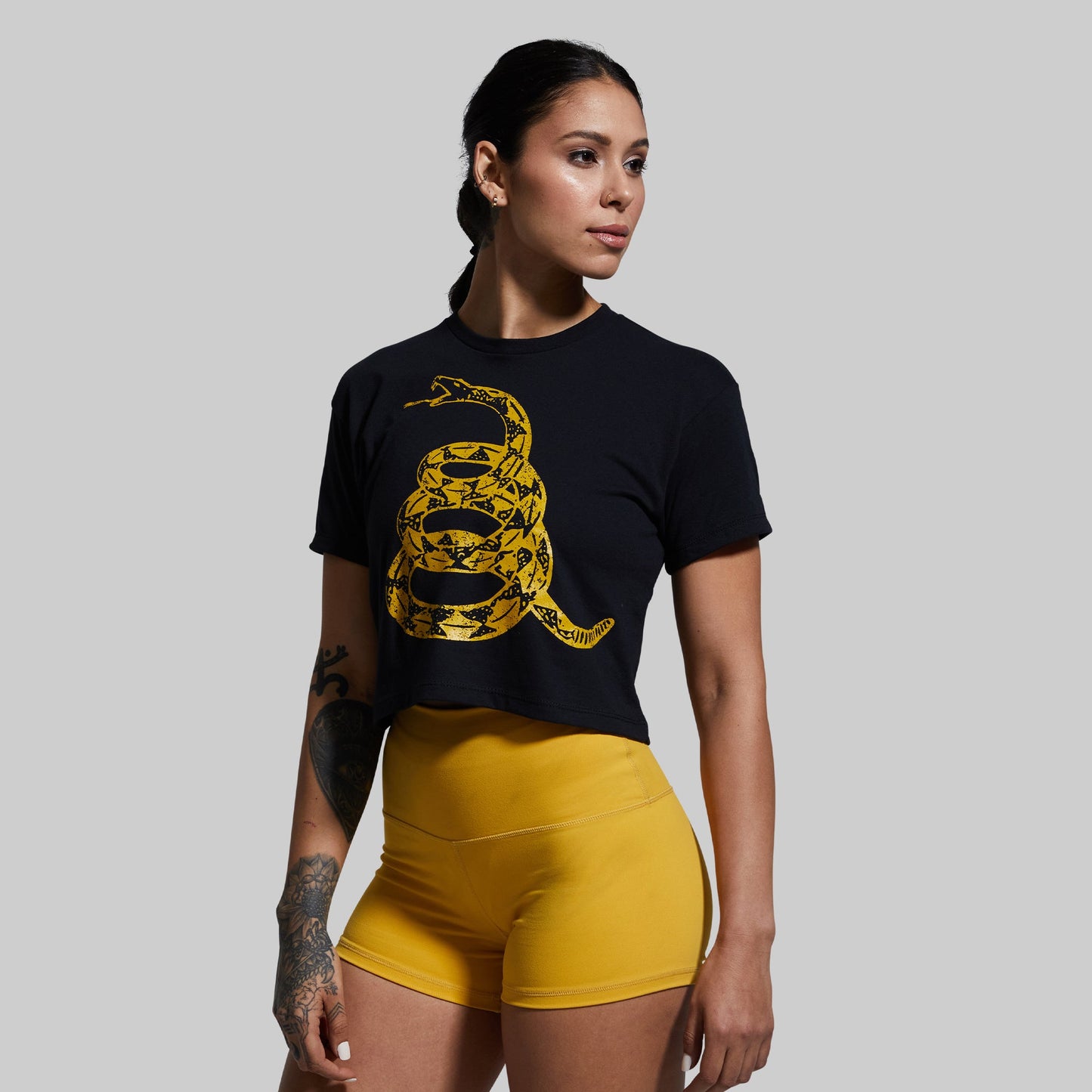 Woman wearing a black t-shirt with a yellow snake design and yellow shorts on a gray background