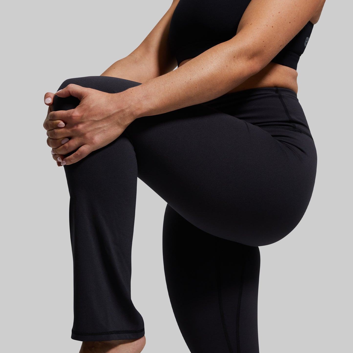 Person wearing black yoga pants stretching on a plain background
