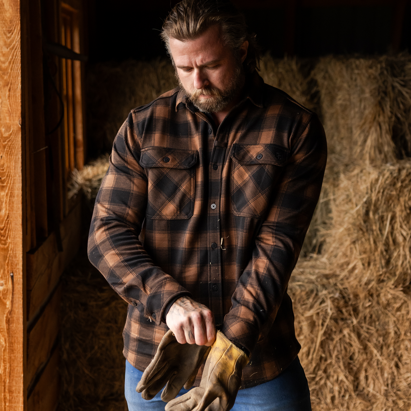 Man in a plaid shirt holding gloves in a barn setting