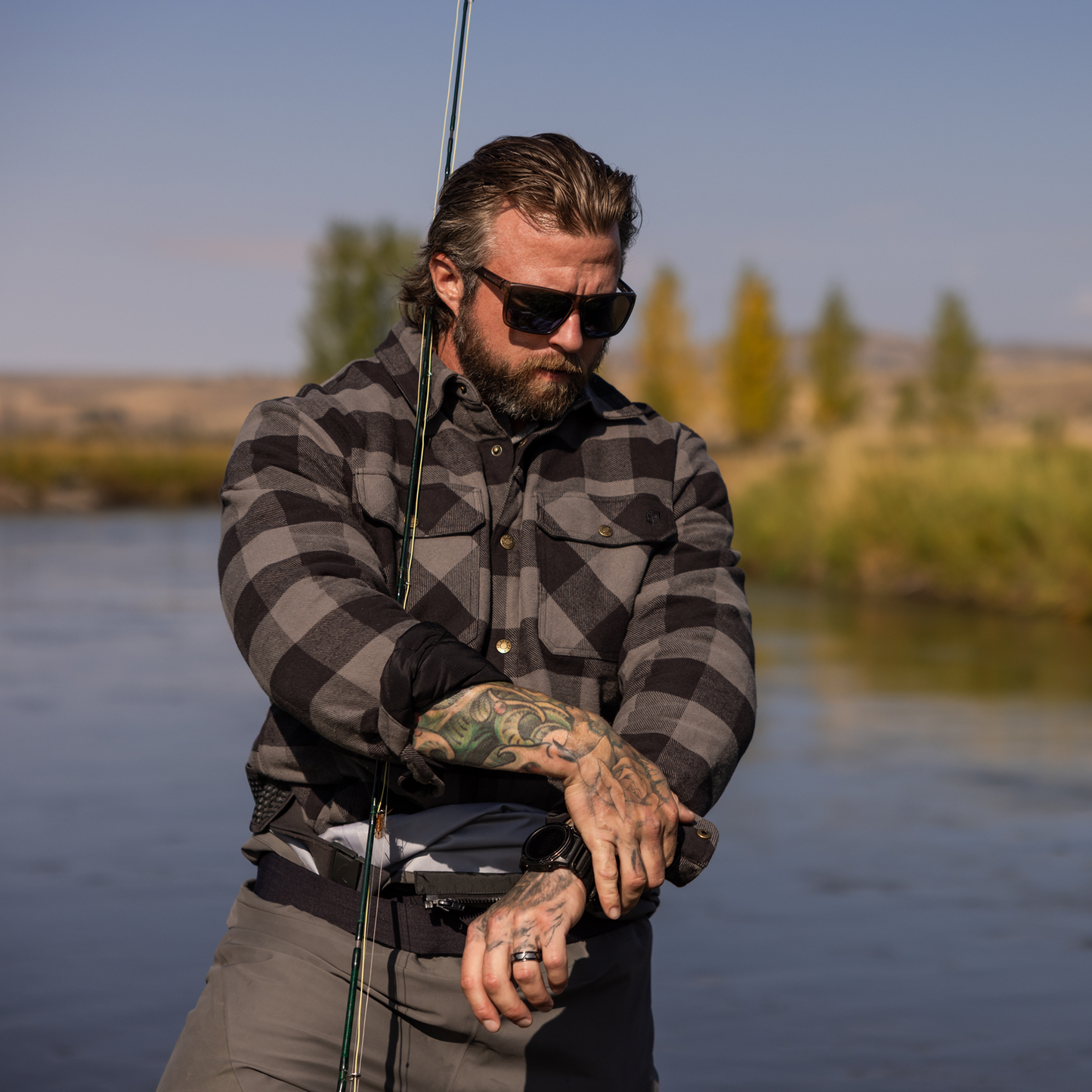 Man with tattoos holding a fishing rod by a body of water