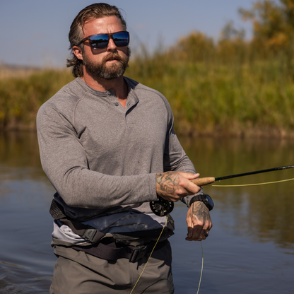 Man fishing by a body of water with sunglasses and a gray shirt.