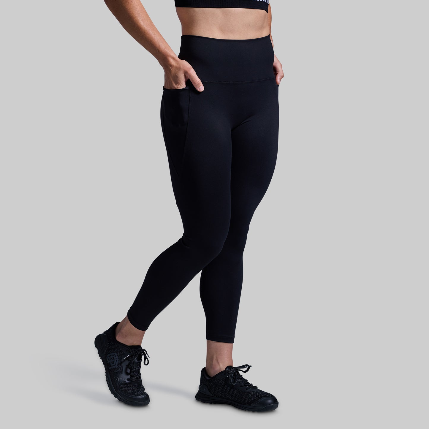 Person wearing black leggings and black sneakers on a gray background