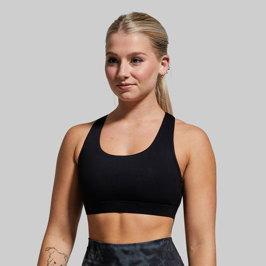 Woman wearing a black sports bra and patterned leggings against a gray background