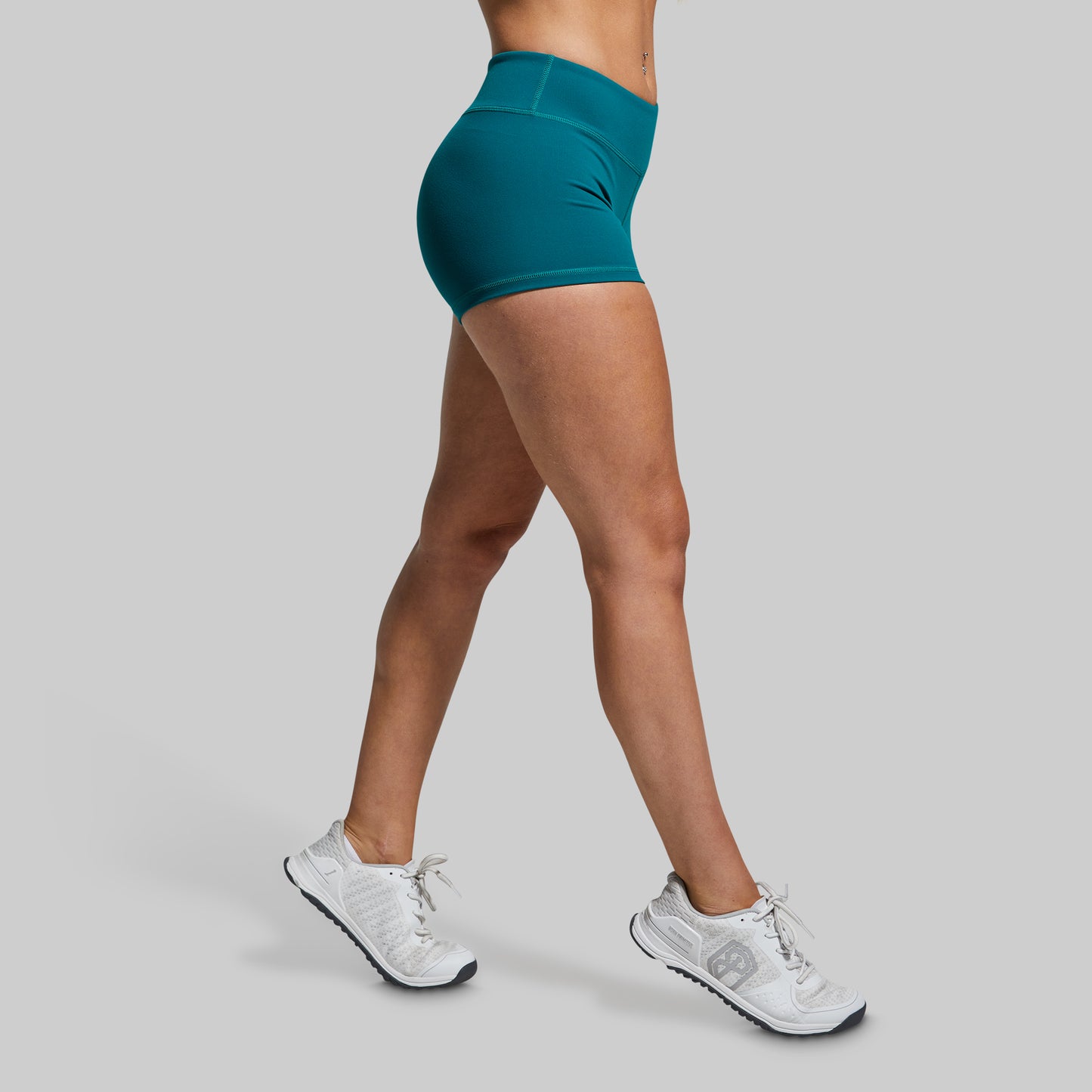 Person wearing teal shorts and white sneakers on a gray background