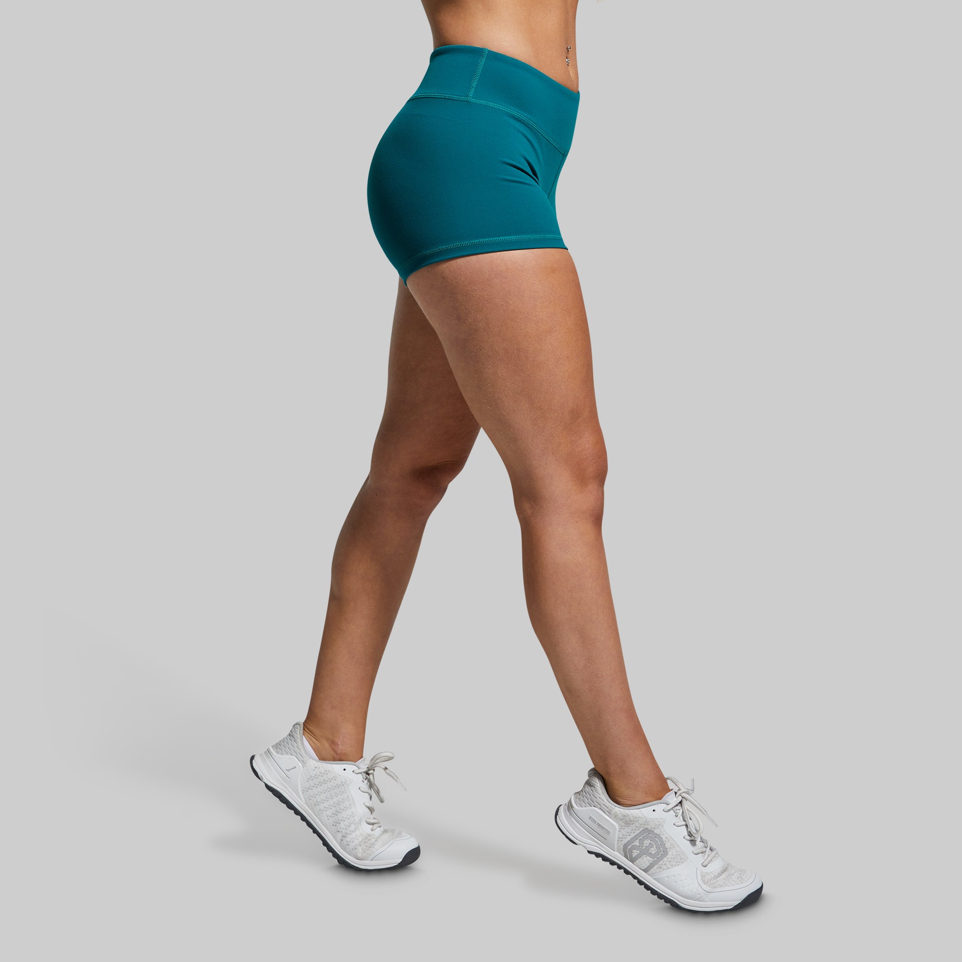 Person wearing teal shorts and white sneakers on a gray background