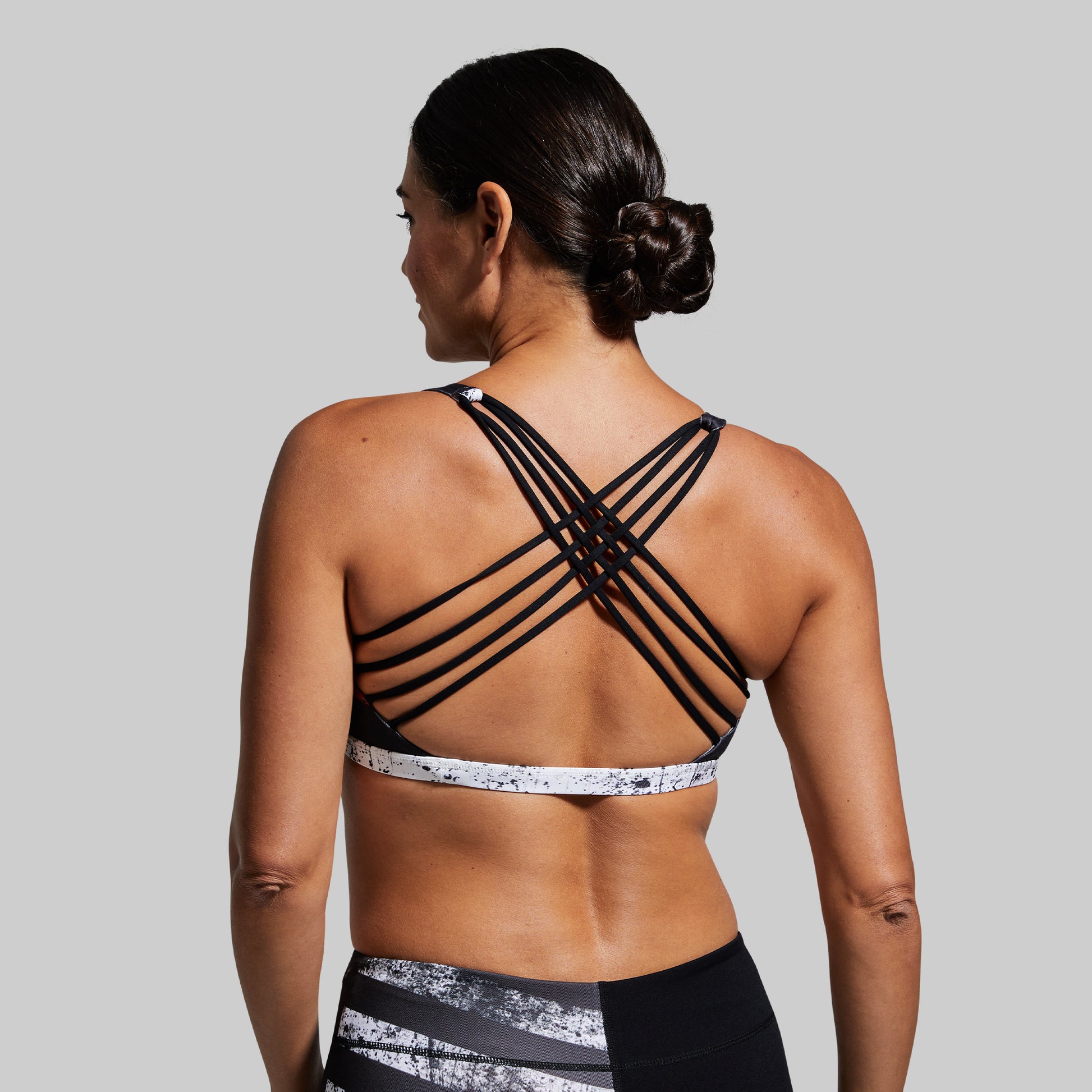 Woman wearing a black sports bra with criss-cross straps on a gray background