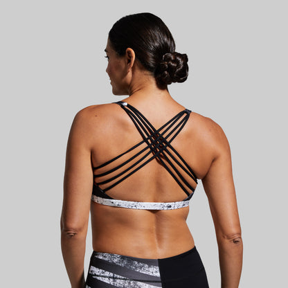 Woman wearing a black sports bra with criss-cross straps on a gray background