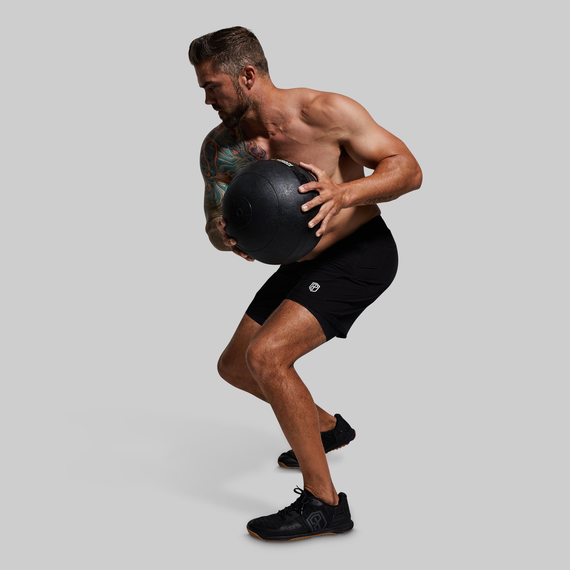 Person holding a medicine ball wearing black athletic shorts with a logo on a gray background