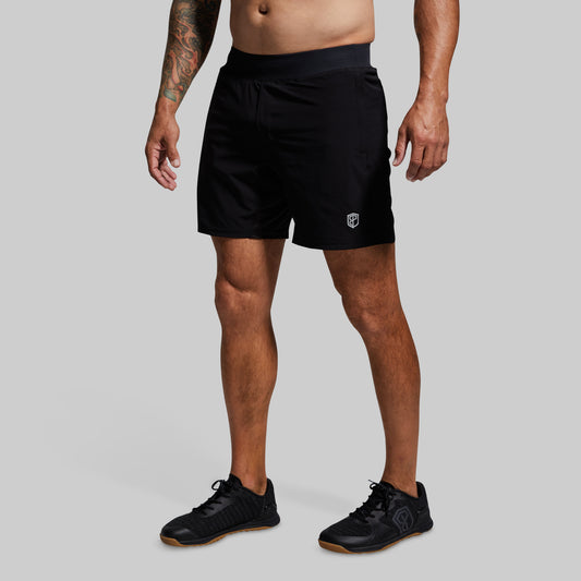 A male model wearing black versatile shorts with a compression liner and a pair of black sneakers.