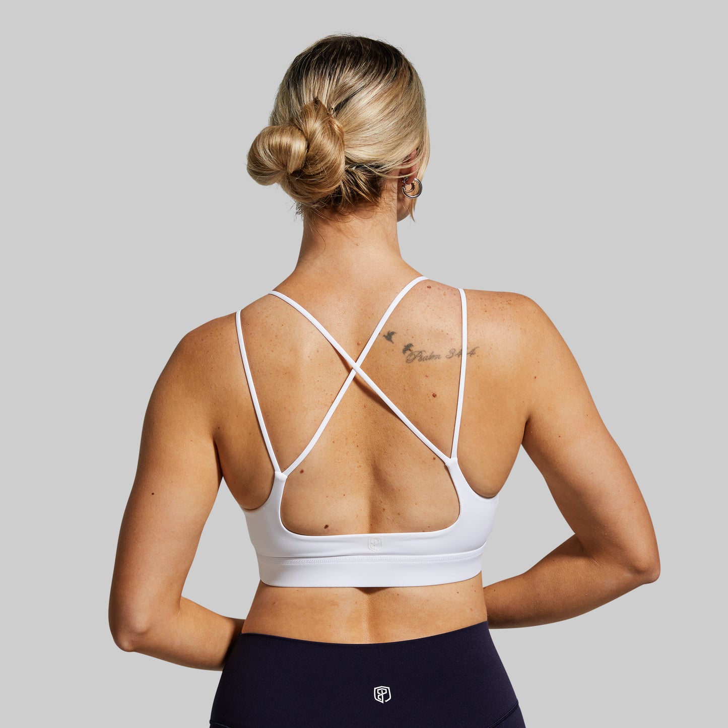 Woman wearing a white sports bra with criss-cross straps on a gray background
