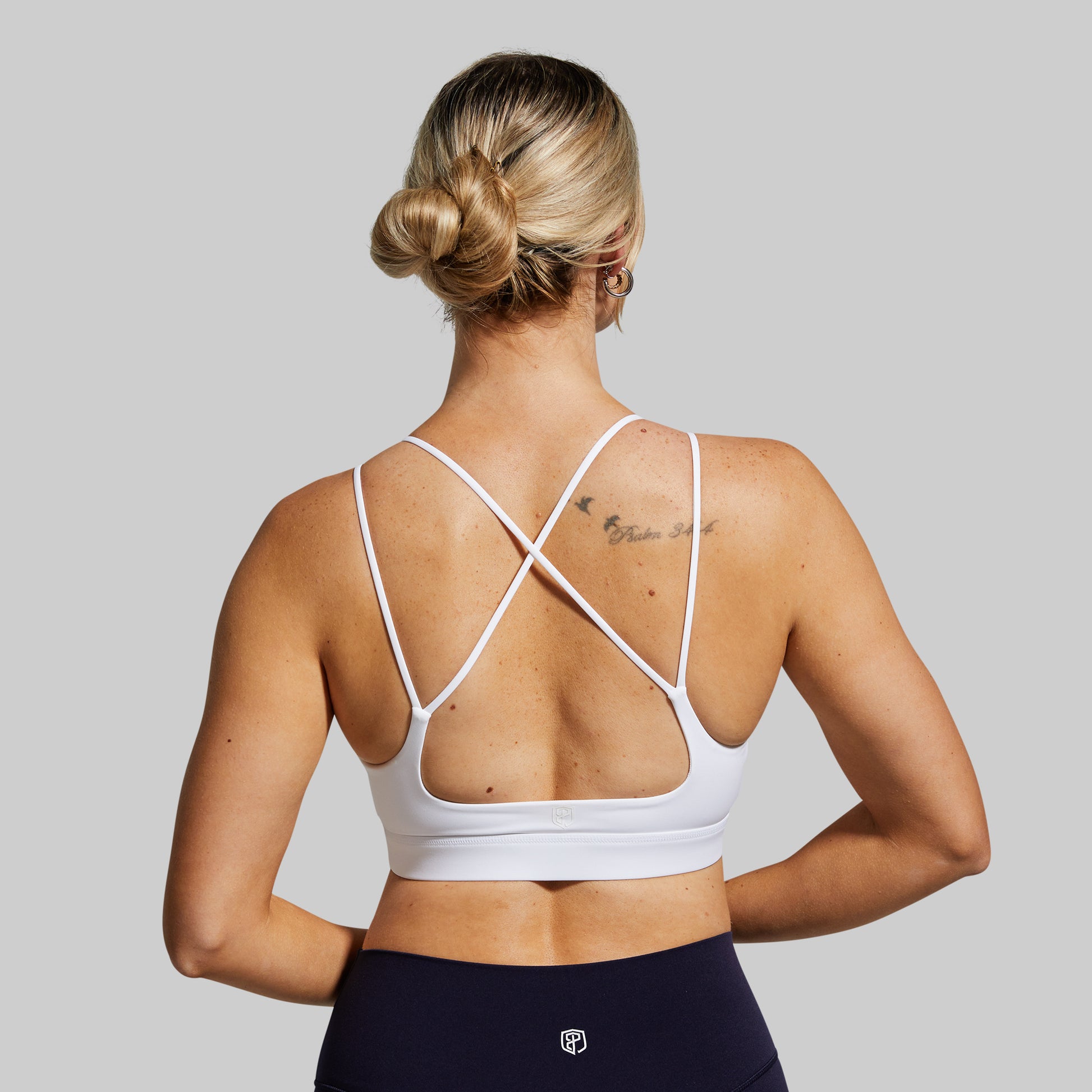 Woman wearing a white sports bra with criss-cross straps on a gray background