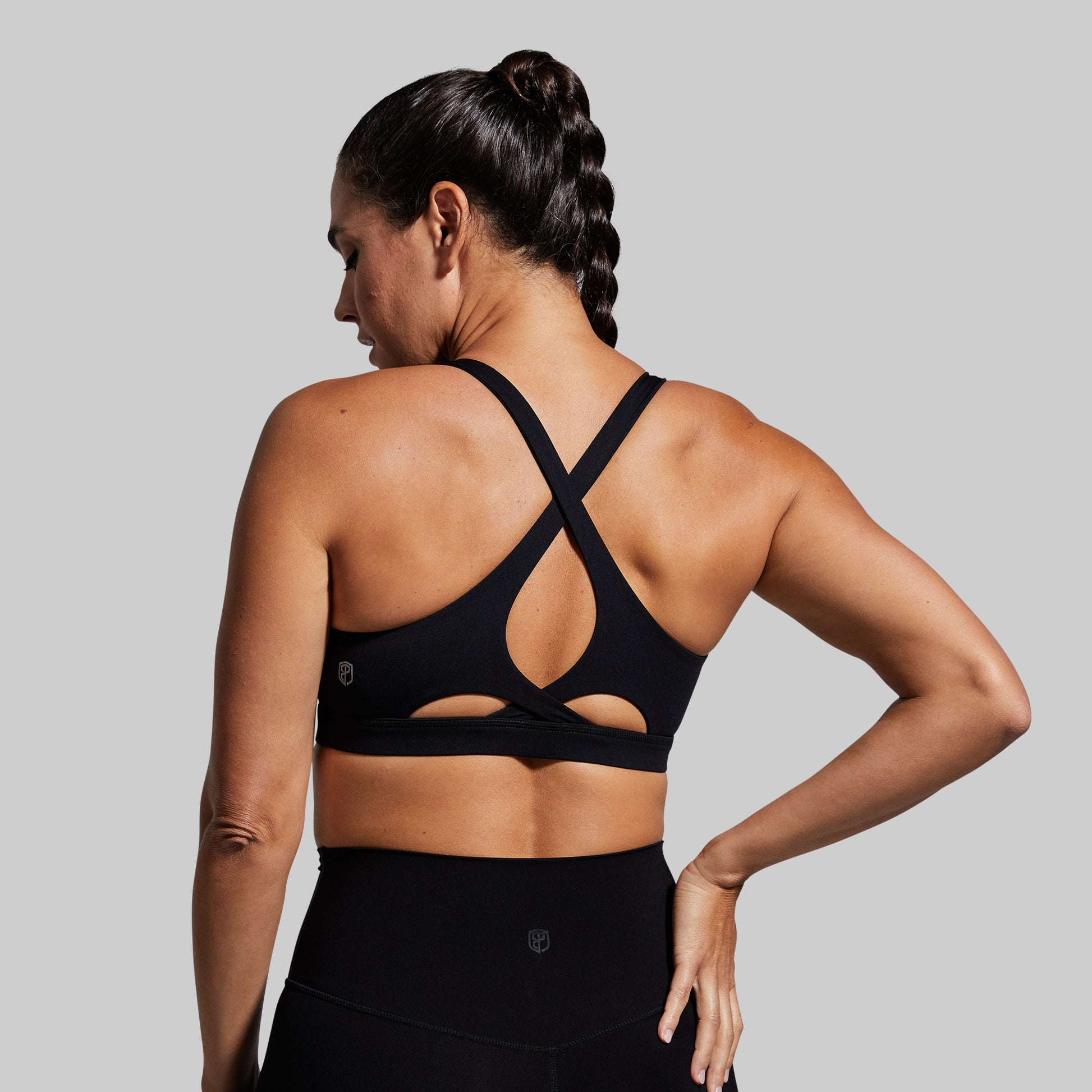 Woman wearing a black sports bra with cut-out design on a gray background