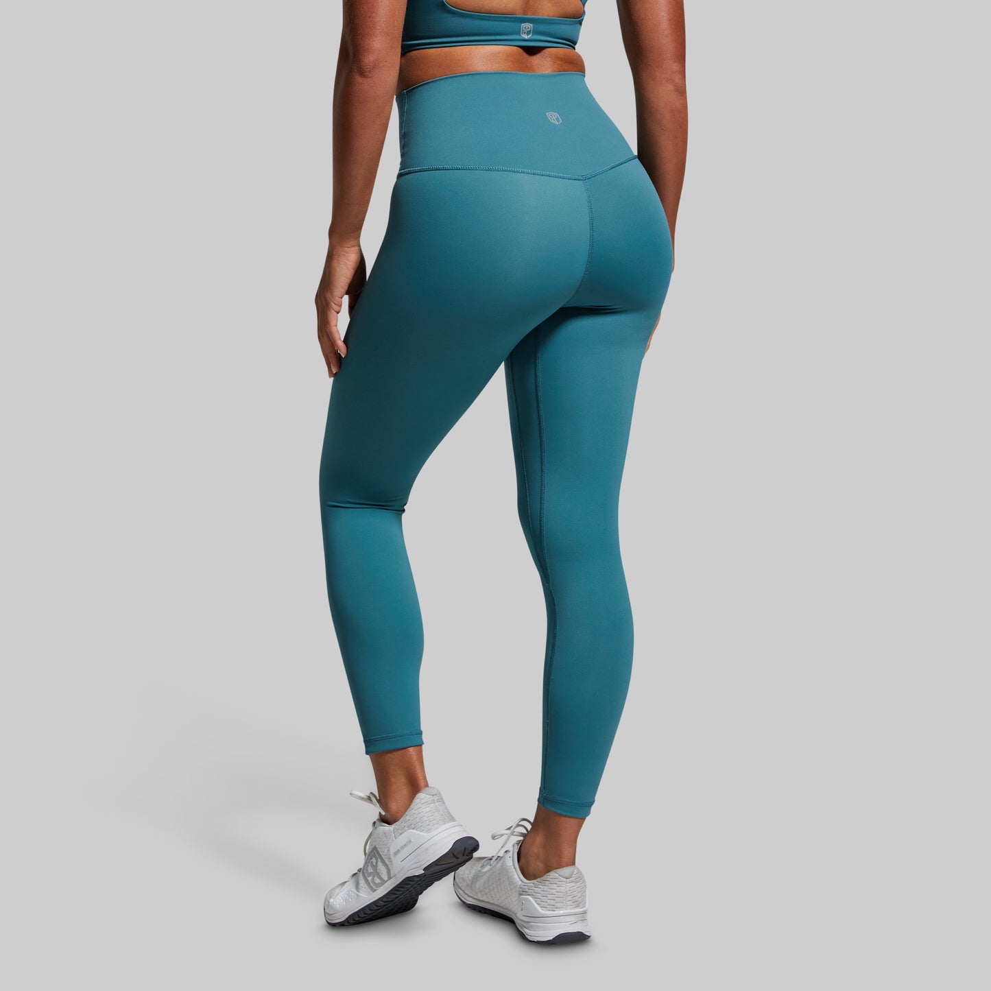 Person wearing teal leggings and a sports bra on a gray background