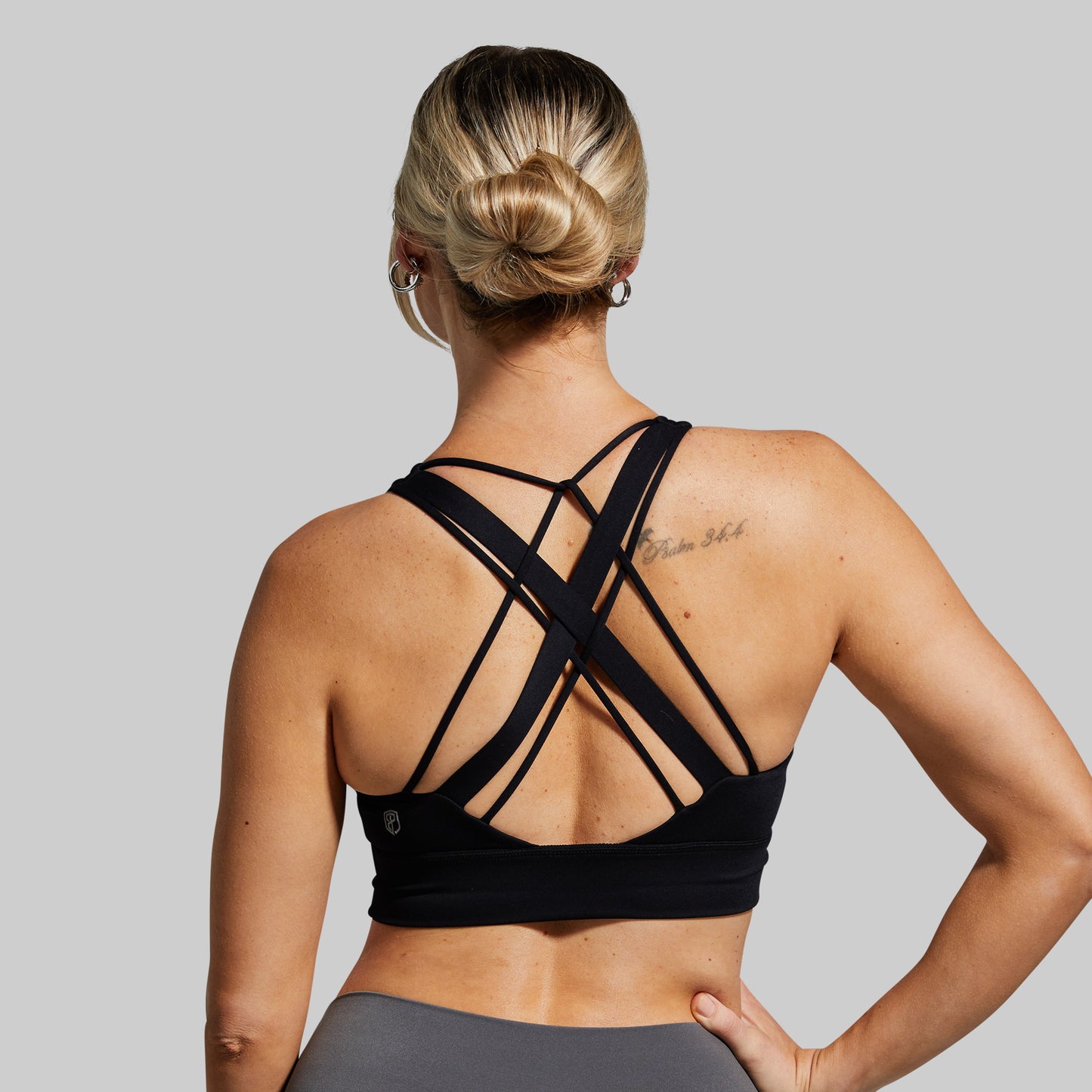 Person wearing a black sports bra with criss-cross straps on a gray background