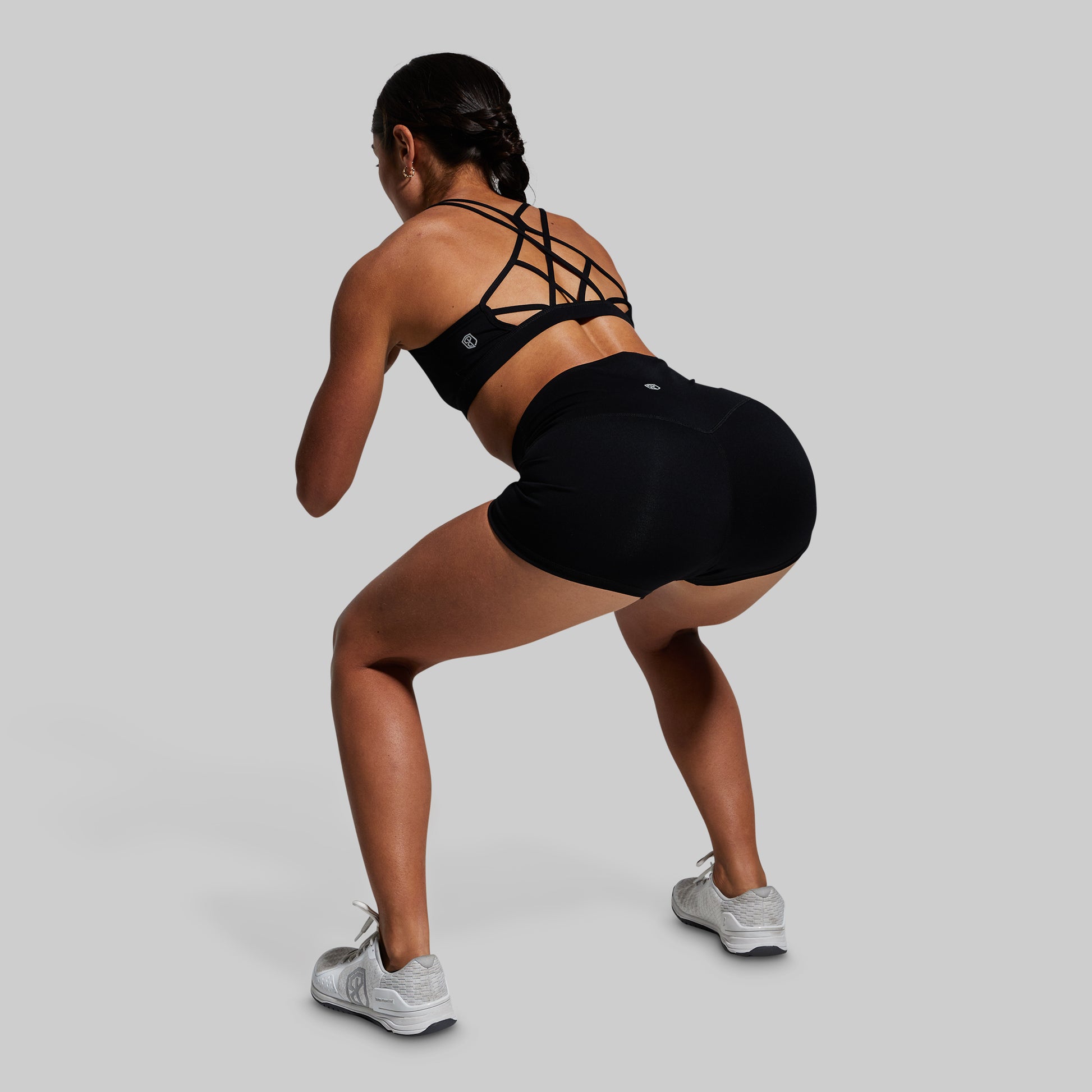 Person wearing a black sports bra and shorts, performing a squat on a gray background