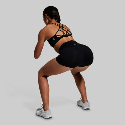 Person wearing a black sports bra and shorts, performing a squat on a gray background