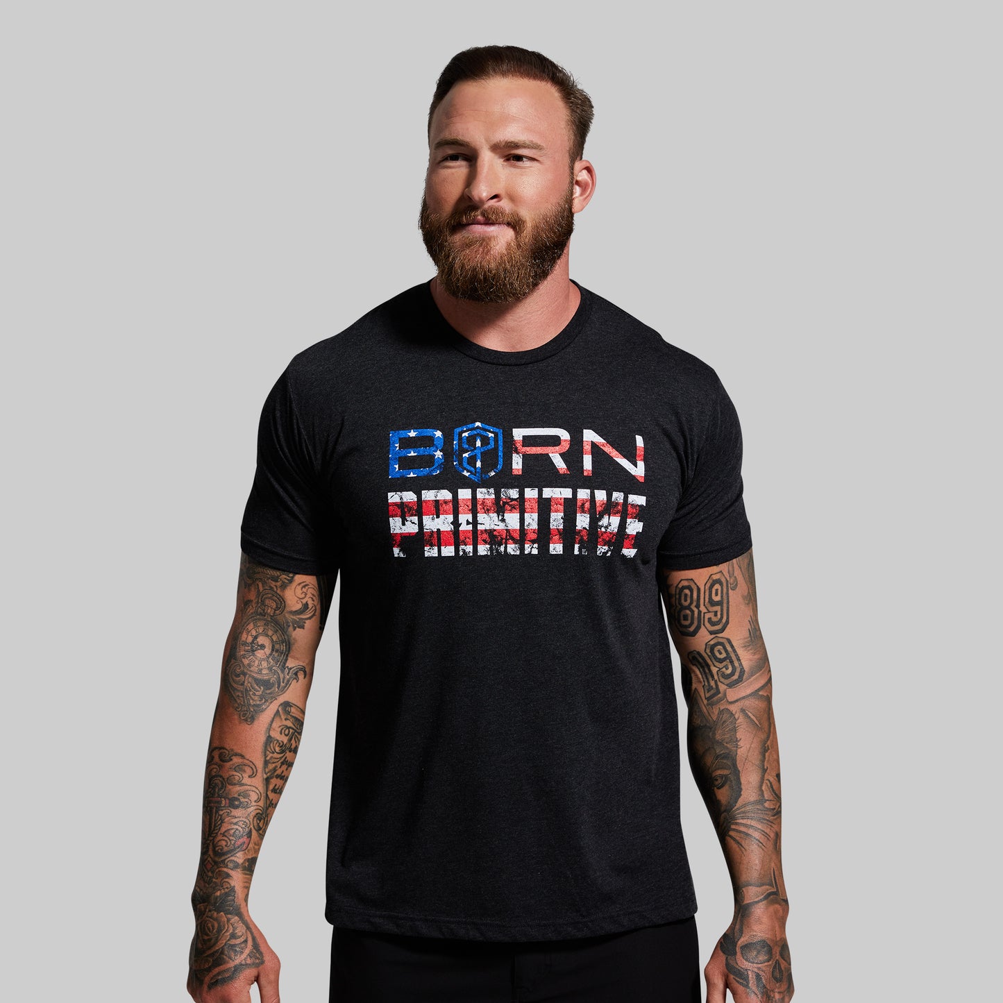Man wearing a black t-shirt with 'Born Primitive' text on a gray background