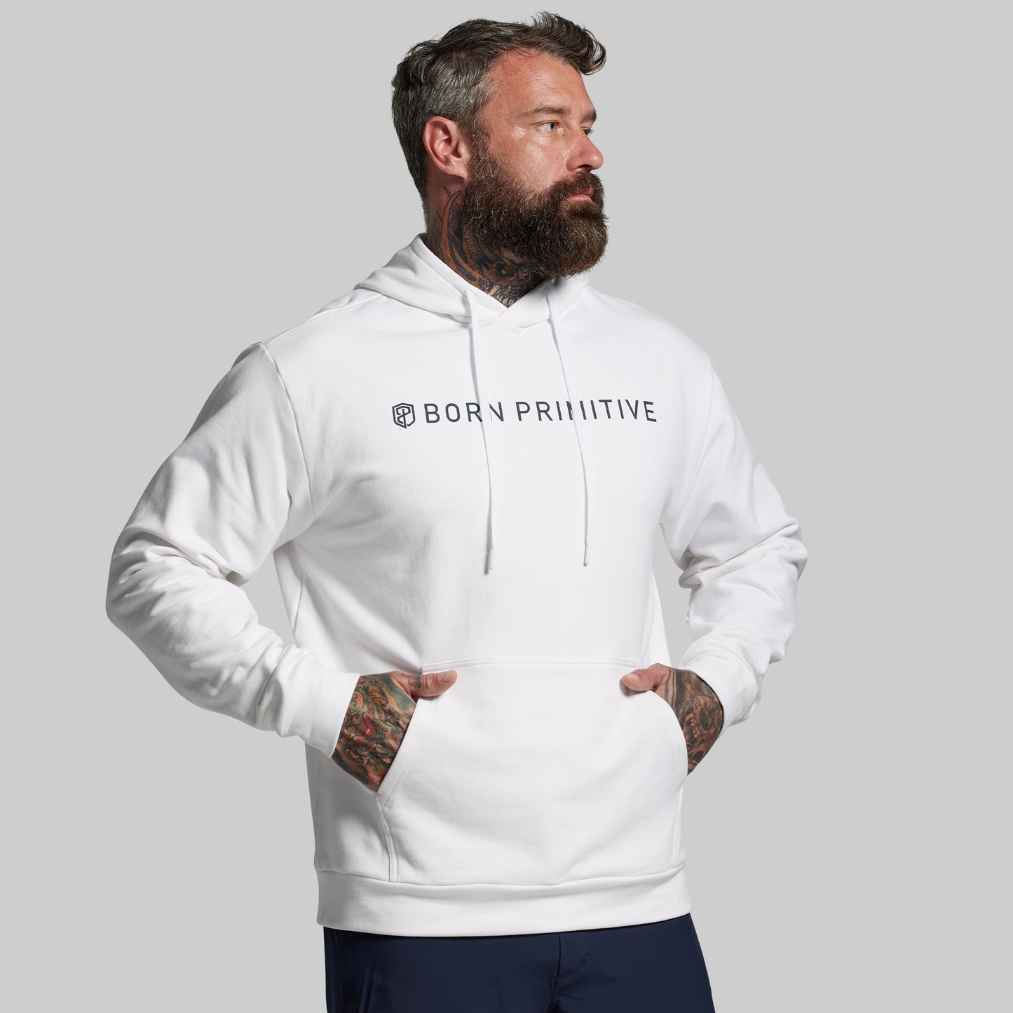 Man wearing a white hoodie with 'Born Primitive' logo on a gray background