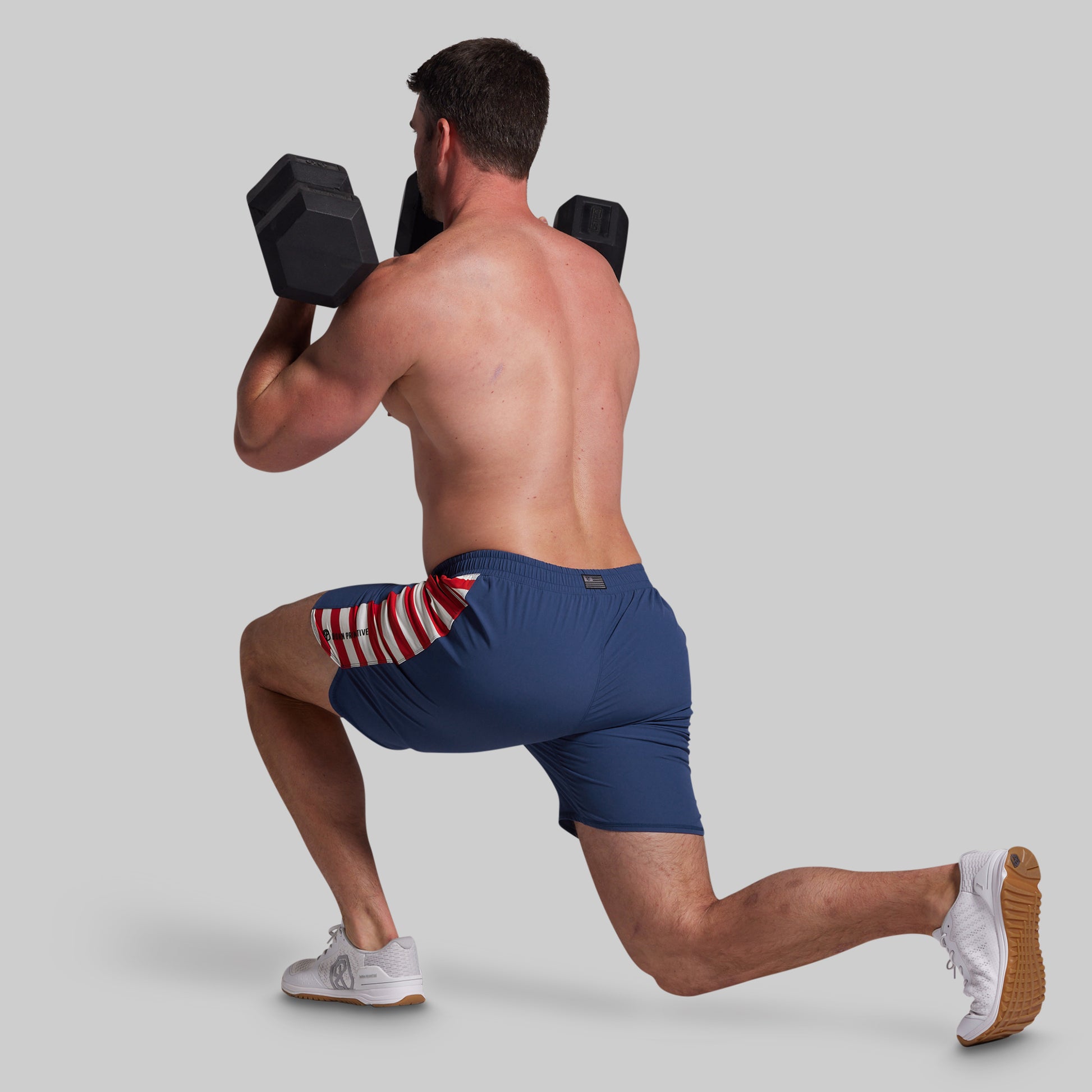 Man performing a lunge with dumbbells wearing blue shorts with a red, white, and blue pattern.