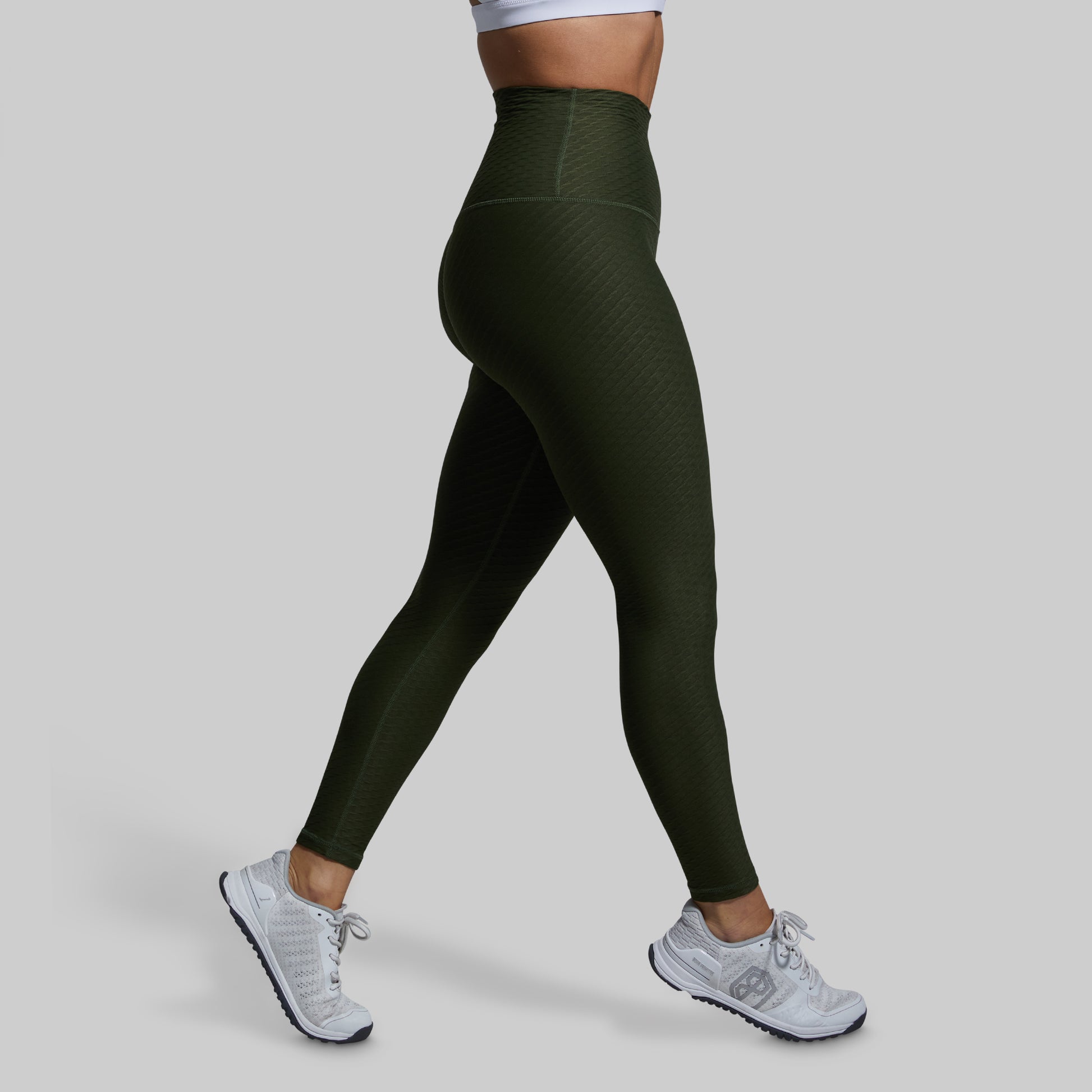 Person wearing green leggings and white sneakers on a gray background