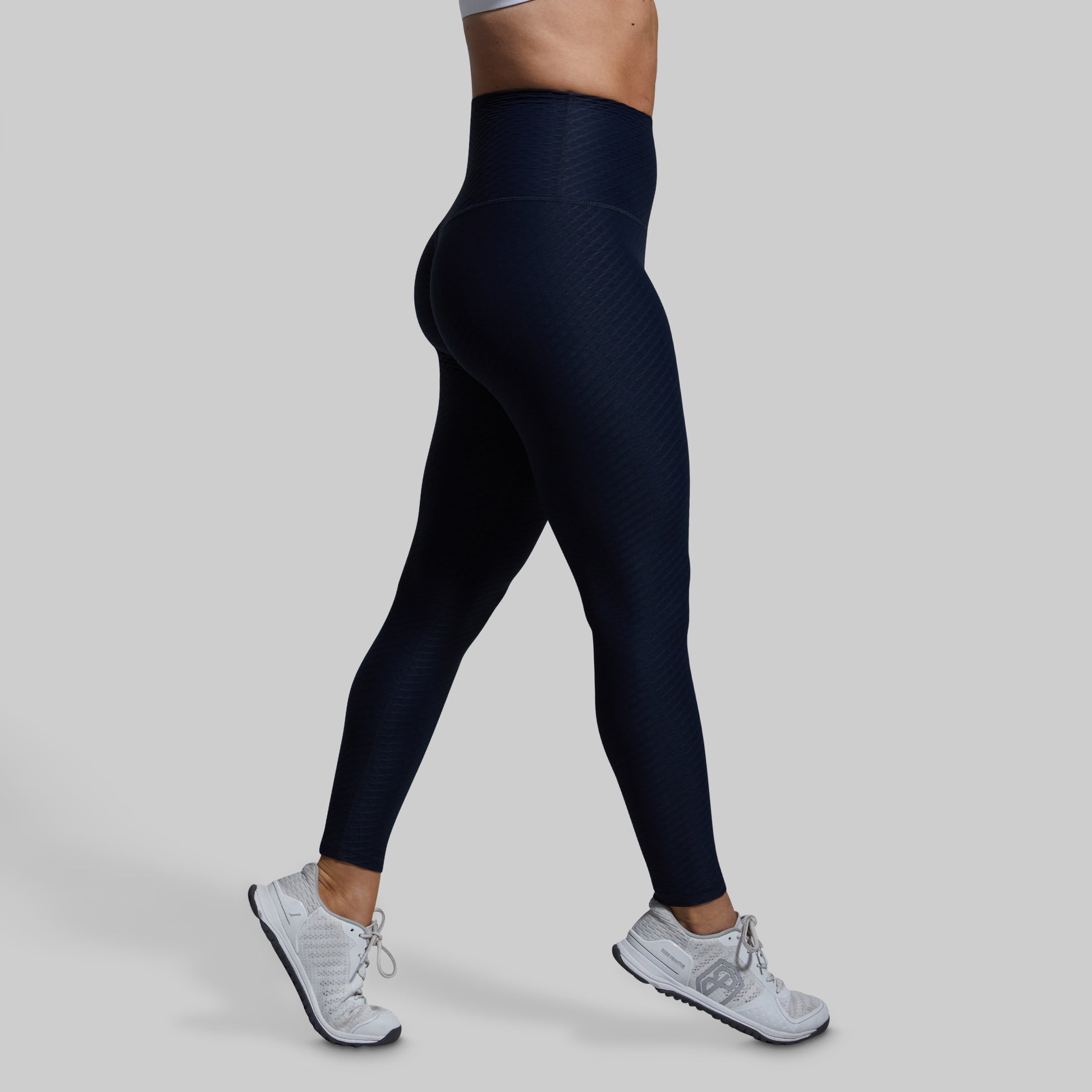 Person wearing blue leggings and white sneakers on a gray background