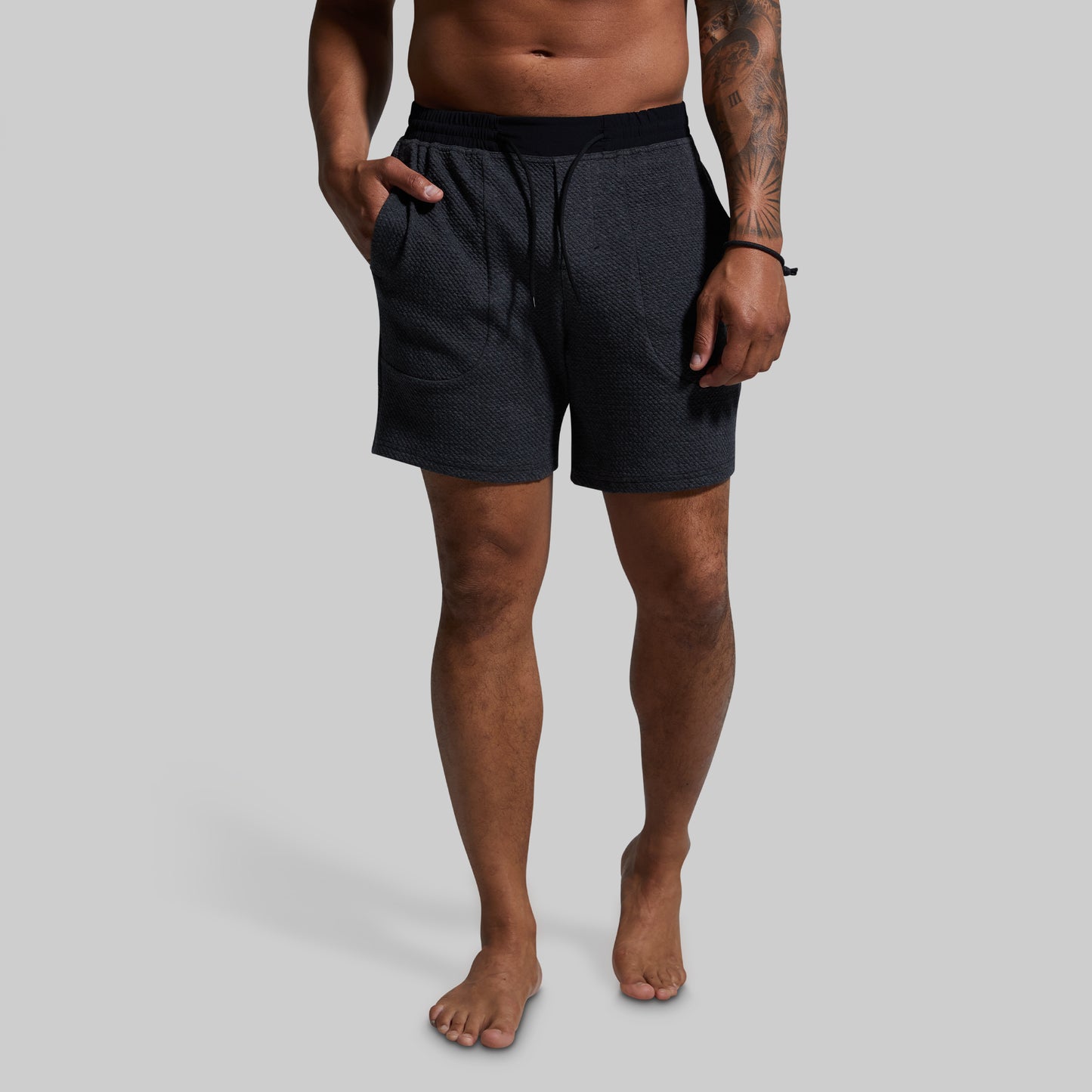 Man wearing dark gray shorts on a gray background
