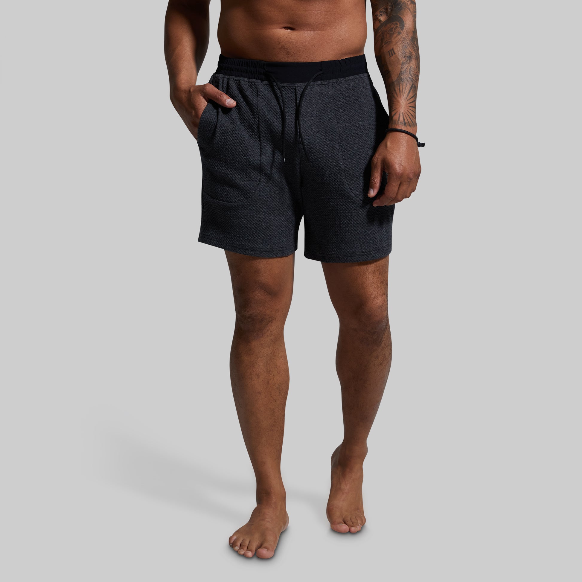 Man wearing dark gray shorts on a gray background