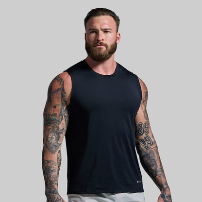 Man wearing a black sleeveless shirt with tattoos on arms against a plain background