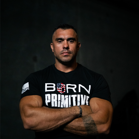 Man wearing a black t-shirt with 'Born Primitive' logo on a dark background