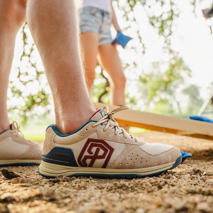 Close-up of a beige and blue athletic shoe with a brand logo on a natural ground surface.