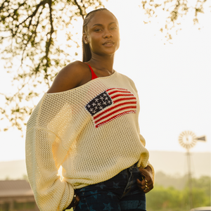 Woman wearing a beige sweater with an American flag design outdoors.