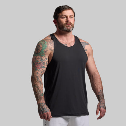 Man wearing a black tank top with tattoos on arms against a gray background