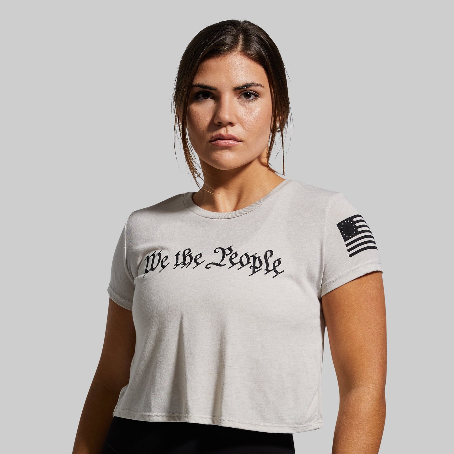 Woman wearing a white t-shirt with 'We the People' text and a flag design on a gray background
