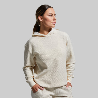 Woman wearing a cream-colored hoodie and pants against a plain background