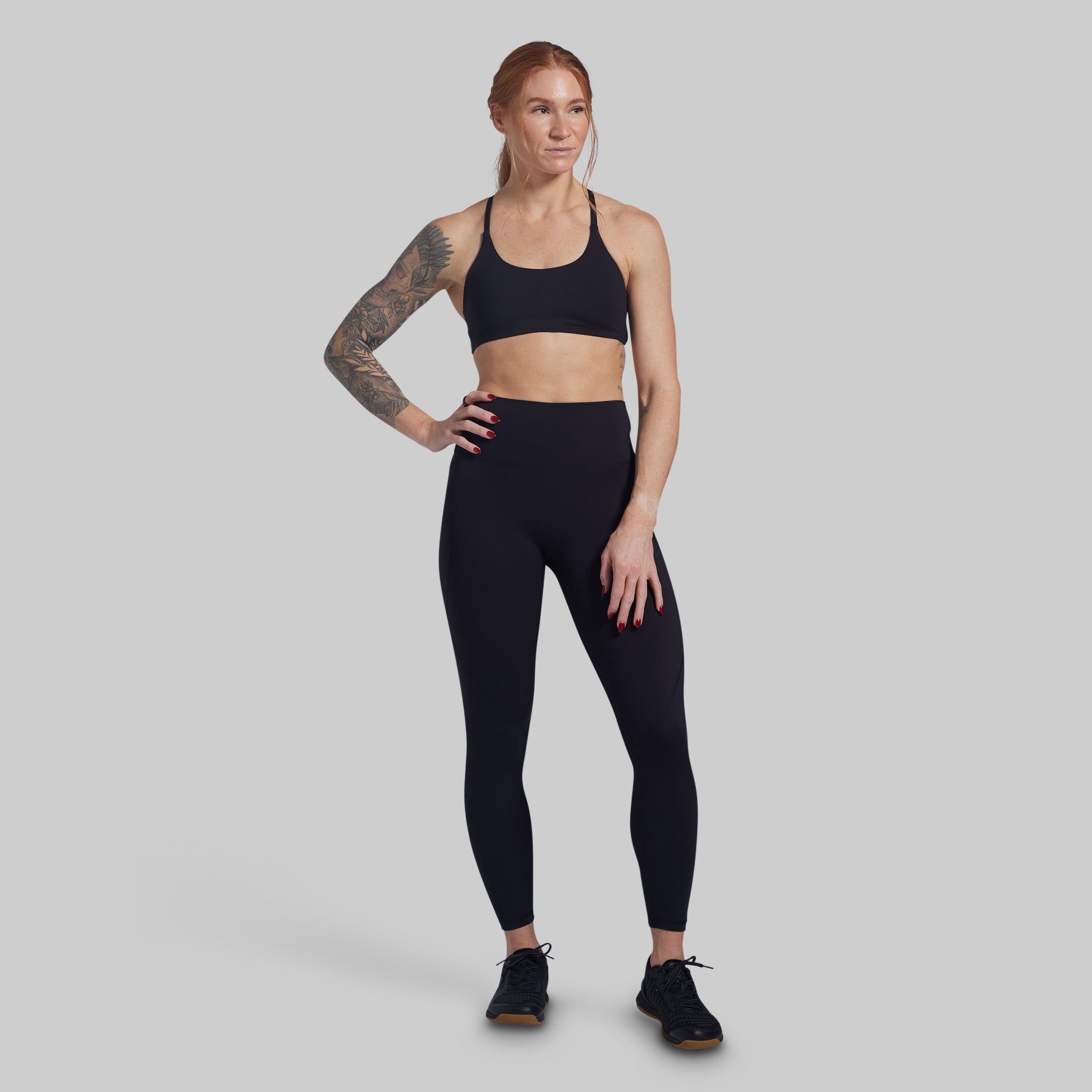 Woman wearing a black sports bra and leggings on a gray background