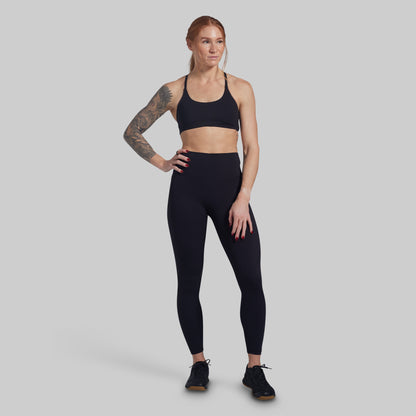 Woman wearing a black sports bra and leggings on a gray background
