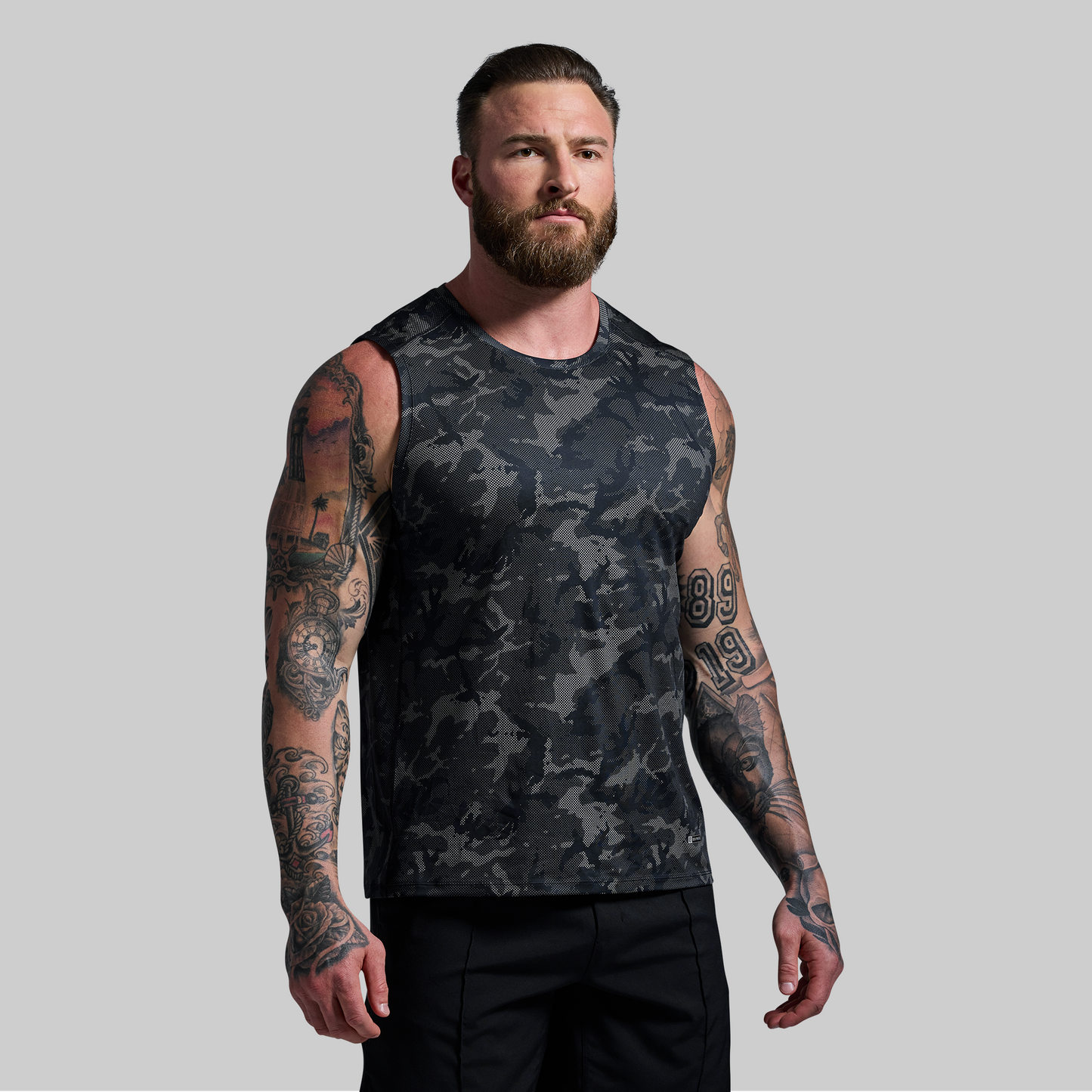 Man wearing a camouflage sleeveless shirt against a plain background