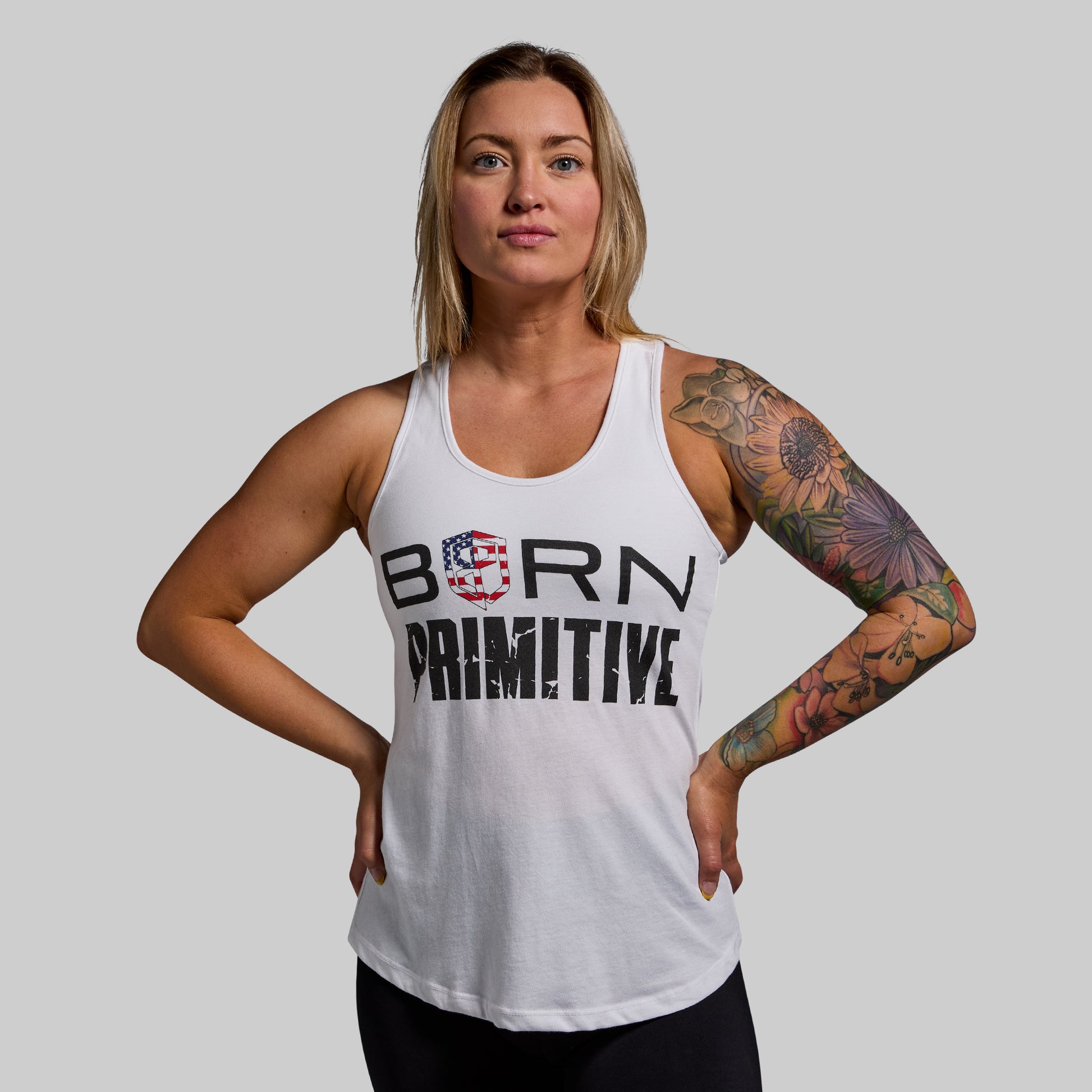 Woman wearing a white tank top with 'BORN PRIMITIVE' text on a gray background