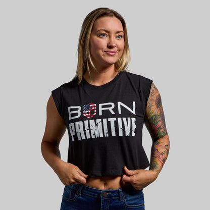 Woman wearing a black sleeveless shirt with 'Born Primitive' text, standing against a plain background