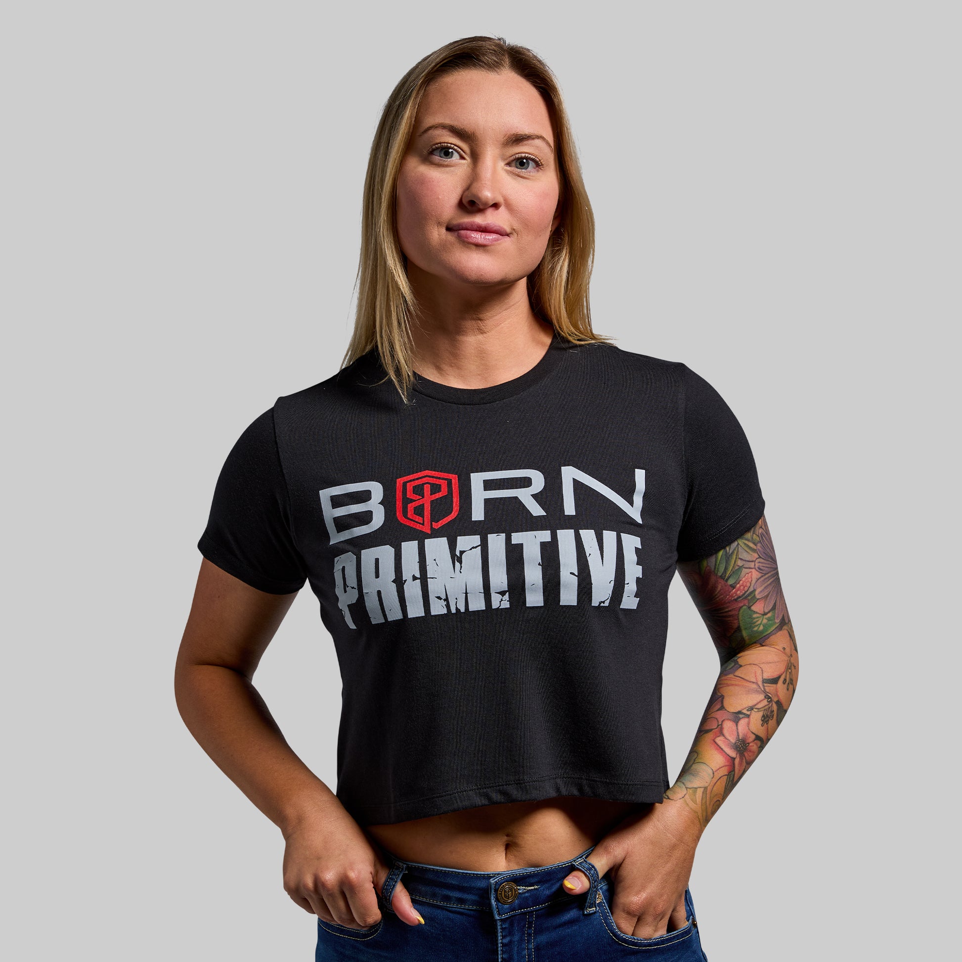Person wearing a black 'Born Primitive' t-shirt on a gray background