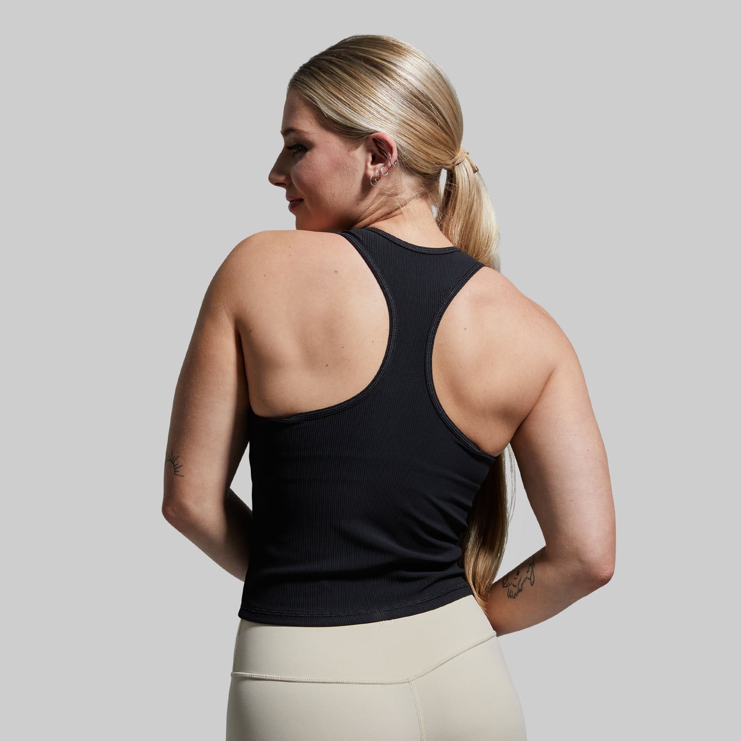 Woman wearing a black tank top and beige leggings against a gray background