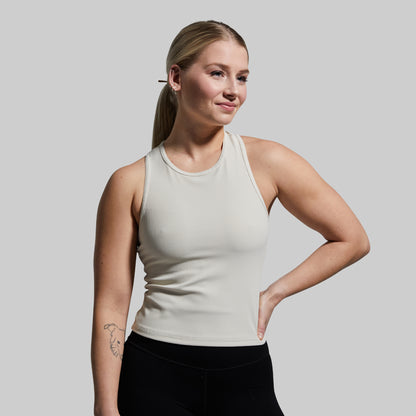 Woman wearing a beige tank top and black pants against a plain background