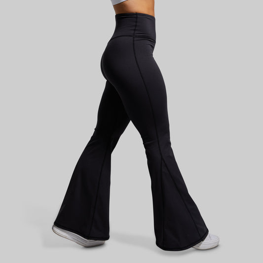 Black flared pants worn by a person on a gray background