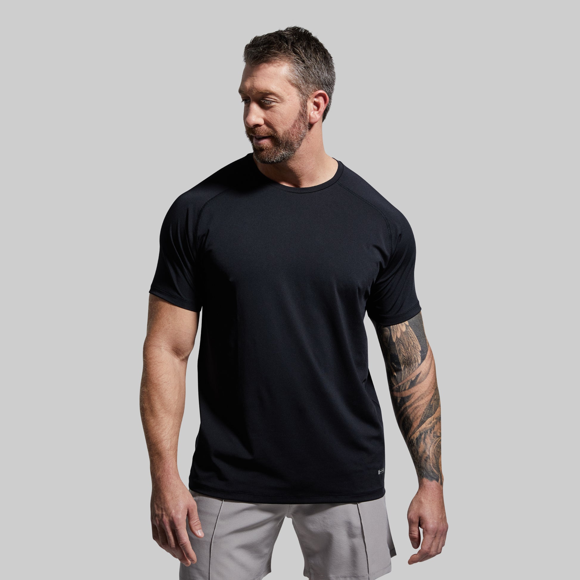 Man wearing a black t-shirt and gray pants against a plain background