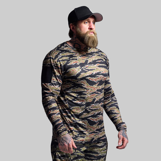 Man wearing a camouflage long-sleeve shirt and black cap on a gray background