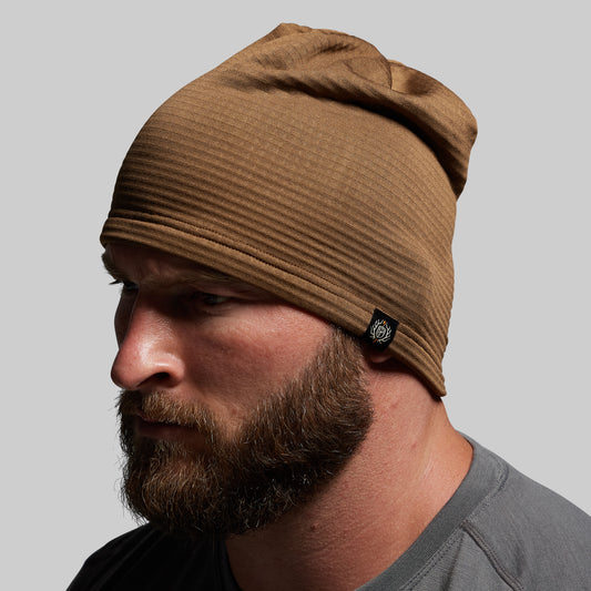 Man wearing a brown beanie with a brand logo on a gray background