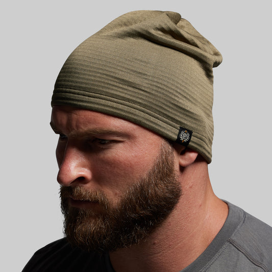 Man wearing a green beanie with a brand logo on a gray background