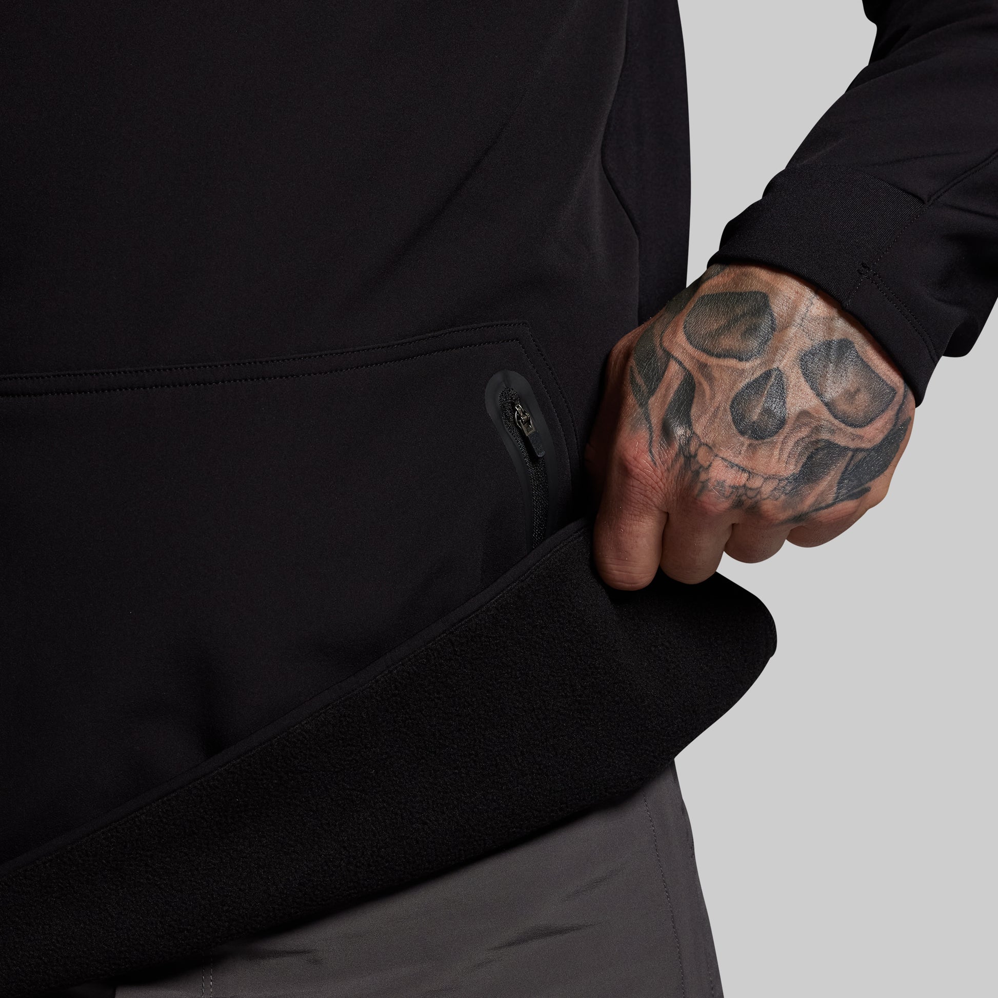 Person wearing a black jacket with a tattooed hand on a gray background
