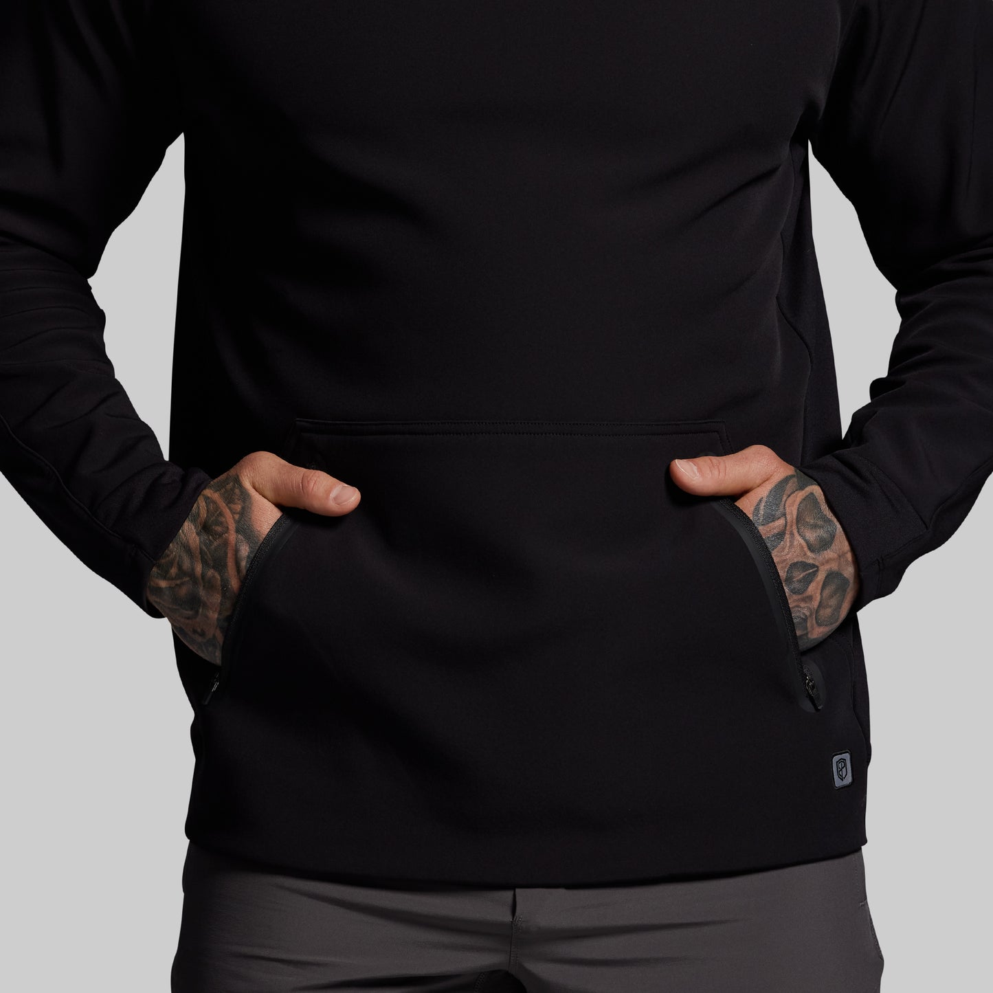 Person wearing a black jacket with tattoos on arms against a gray background